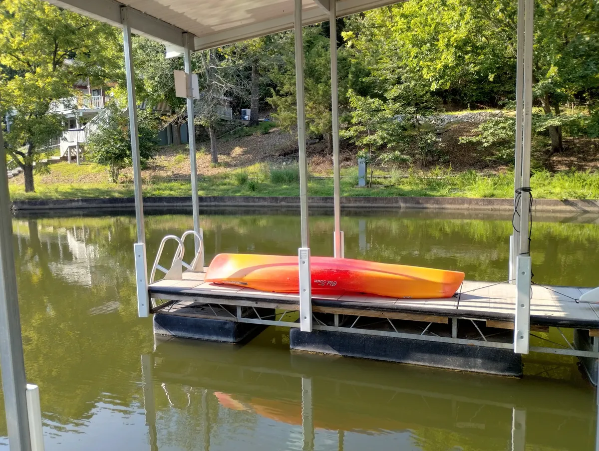 A bright kayak sits on the private dock, surrounded by calm lake water and lush greenery. The dock extends into the gentle cove, inviting for both relaxing and launching water adventures. The scene radiates tranquility and highlights both the dock and water-based activities.