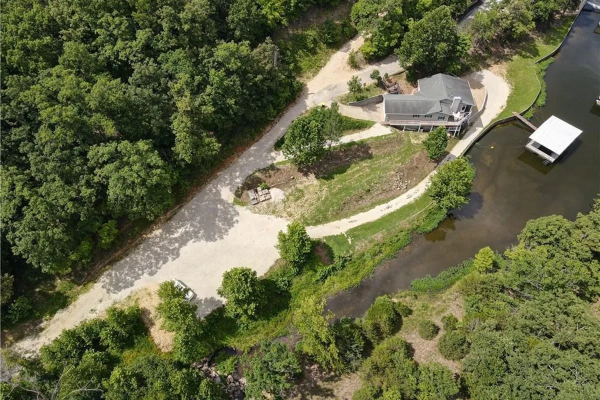 An exterior view of the house, situated right on the waterfront, with a driveway winding through the trees. The lakeshore setting and ample yard space are evident, suggesting safe, scenic spots for on-leash pet play and relaxation in a natural setting.