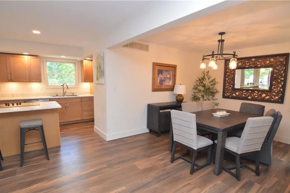 This image showcases a warmly lit interior space featuring a large family-sized dining table, a kitchen island, decorative mirror, and wall art. The setup is ideal for family meals, entertaining guests, and engaging in group activities. The inviting ambiance underlines the communal spirit described in the section.