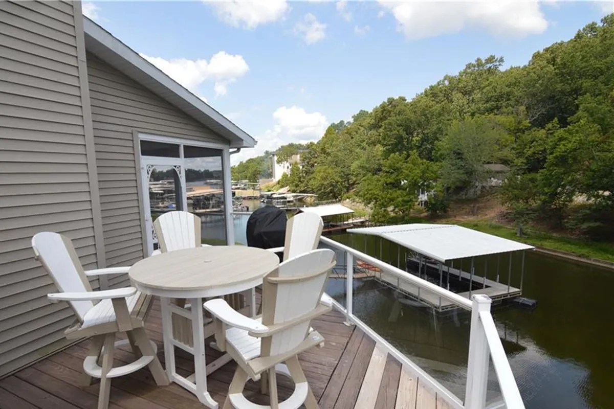 This image features an outdoor dining set positioned on a spacious deck, with a clear view of the lake and lush greenery in the background. The inviting scene suggests a space perfect for al fresco meals, relaxing afternoons, or gathering with friends and family while taking in the natural beauty.