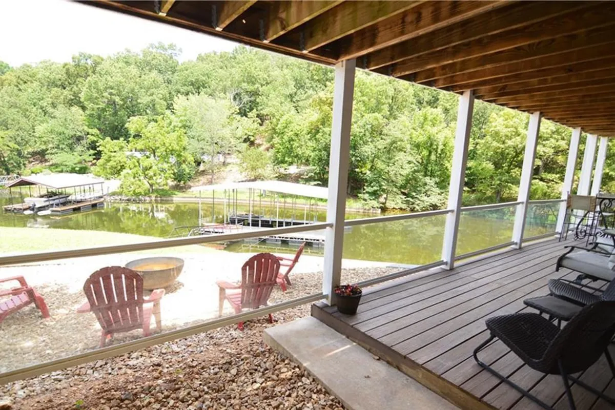 A tranquil lakeside setting featuring red Adirondack chairs overlooking a private dock, surrounded by natural greenery and calm water. The image captures a clear view of the waterfront with easy access to the dock and open water, inviting visitors to relax, fish, or prepare for a boating adventure.