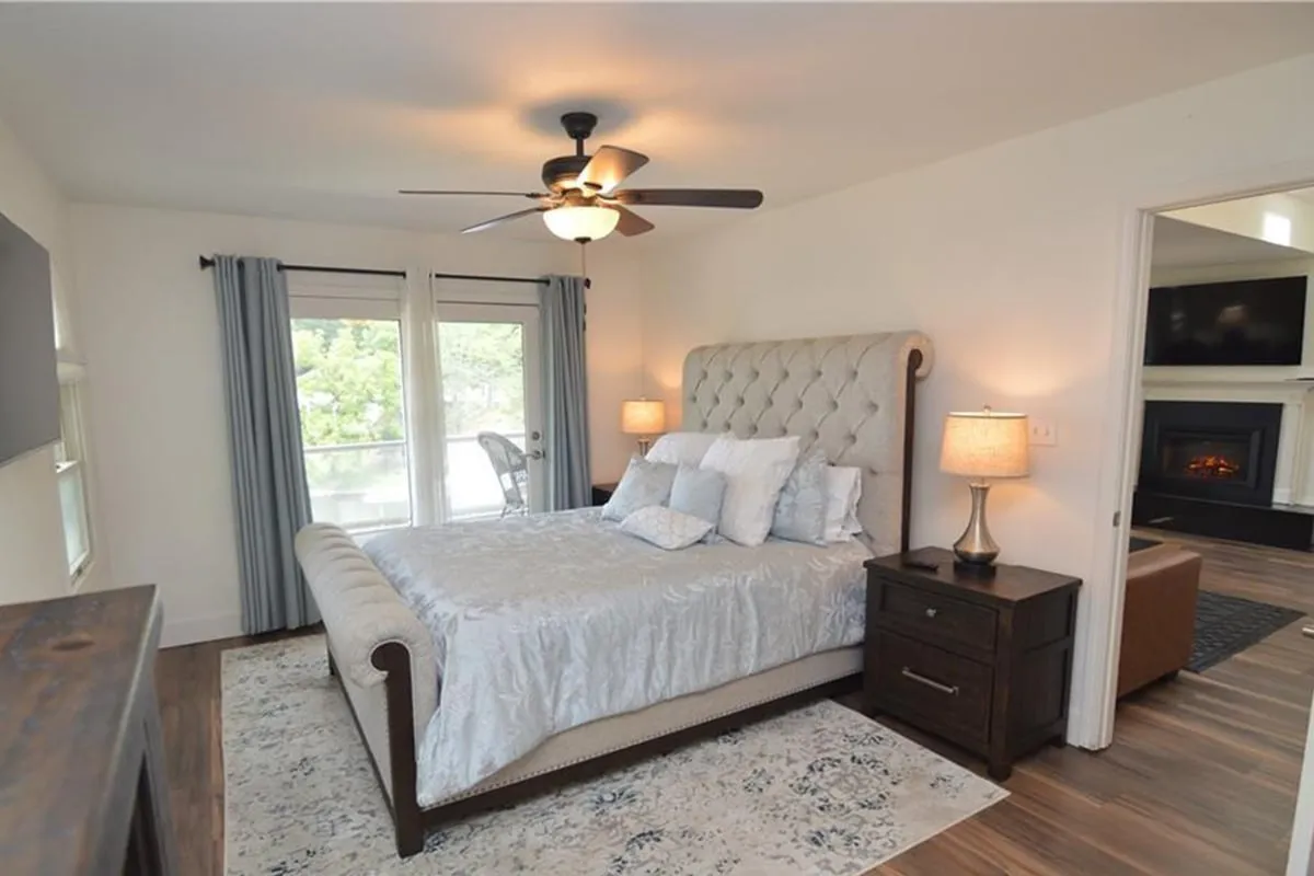 This image features a serene bedroom with a tufted headboard, large windows letting in abundant natural light, and nightstands with lamps on either side. The overall decor is calming, with neutral tones and a sense of comfort that invites relaxation. The spaciousness and the ambient lighting create a peaceful retreat ideal for unwinding.