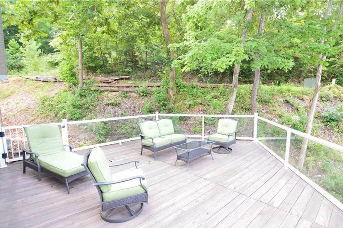 Here, a set of green chairs surrounds a glass-topped table on a wooden deck, embraced by surrounding trees. The scene radiates calm and invites moments of relaxation, morning coffee, or evening conversation under the stars.