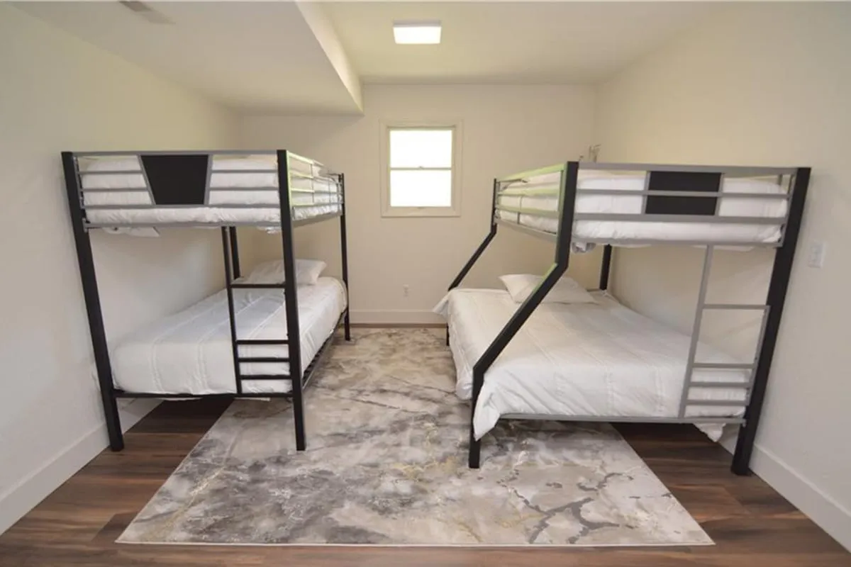 A cozy bedroom with bunk beds, a soft area rug, and natural light streaming through a window. The space feels playful and inviting, making it ideal for families or groups of friends. The arrangement offers flexibility for multiple sleeping options in a comforting, home-like environment.