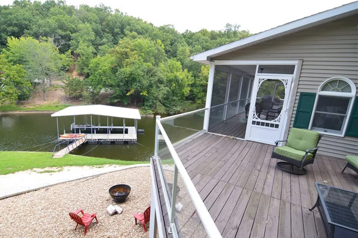 A broad lake view frames a screened porch and red chairs on the dock, with the calm cove waters inviting for kayaking, fishing, or morning exploration. The peaceful setting hints at both active play and quiet relaxation while connecting the house directly to the water.