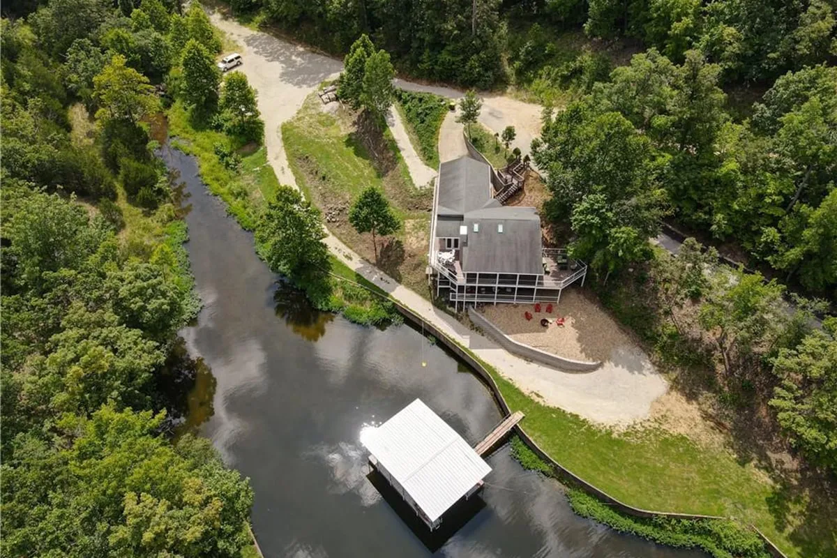 This image features Cordelia's Moonlit Manor set beside the tranquil lake, with the house, private dock, shimmering water, and surrounding trees all in view. The scene illustrates families enjoying activities such as fishing from the dock, boating, and relaxing by the water. A beautiful sunset bathes the area in golden light, evoking a sense of serenity and togetherness.